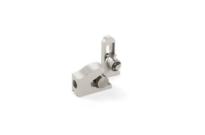 A small, metallic mechanical component with a hinge and adjustable screws, resembling parts used in window actuators, is placed on a white background.