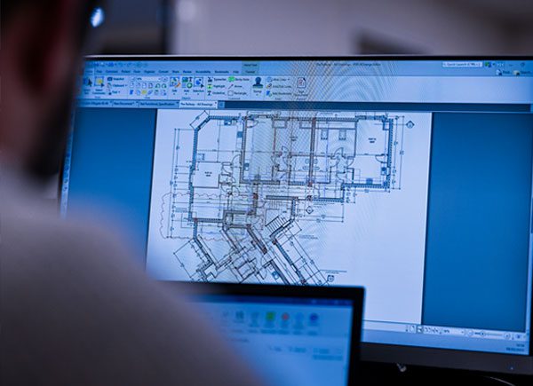 A person reviews architectural blueprints on a computer screen, focusing on detailed floor plans.