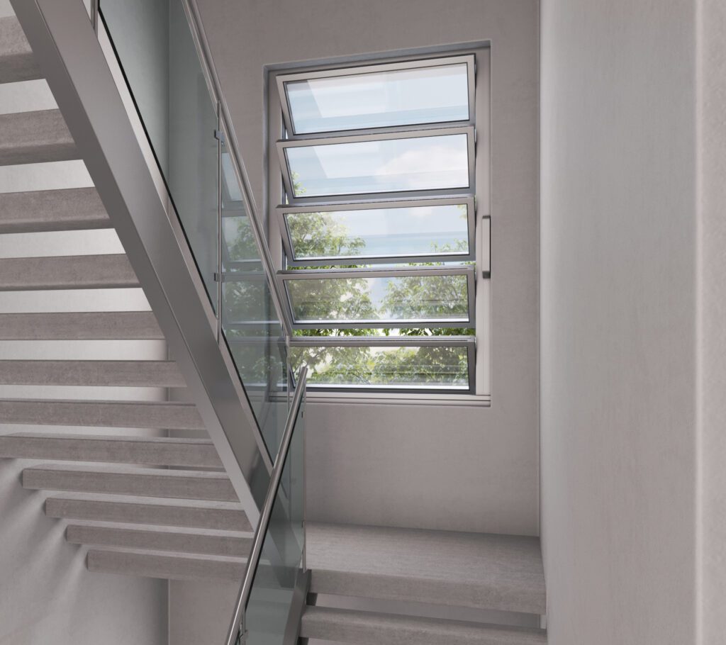 Stairwell with glass railings and modern horizontal windows showing an outdoor view. The walls are light gray, and the stairs are made of concrete.