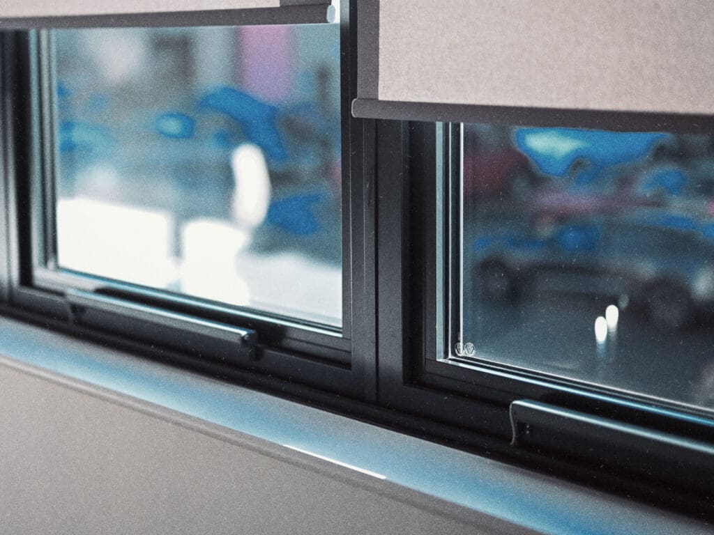 Two closed beige blinds cover the window, with a blurred view of cars and buildings outside. The setup can be easily integrated with window actuators for seamless door automation and improved smoke ventilation in case of emergencies.