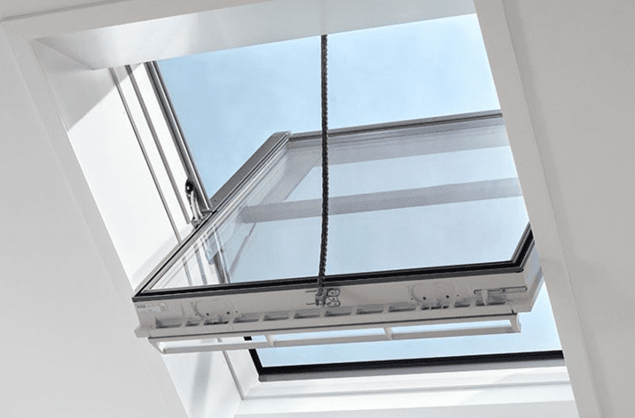 An open skylight window viewed from indoors, equipped with window actuators, reveals a clear blue sky outside.