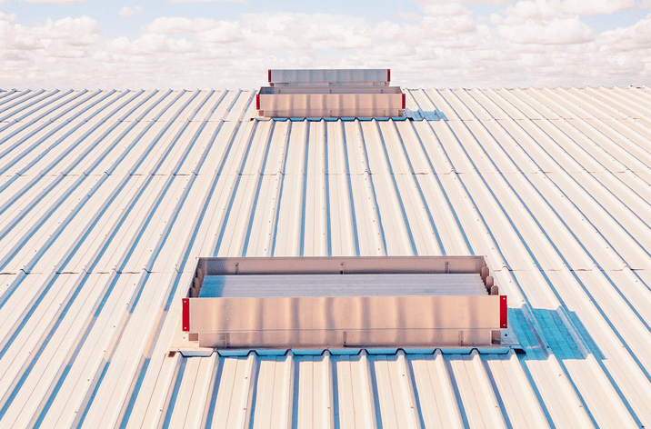 A metal rooftop with two rectangular skylights aligned in a row under a partly cloudy sky, enhanced by natural ventilation.