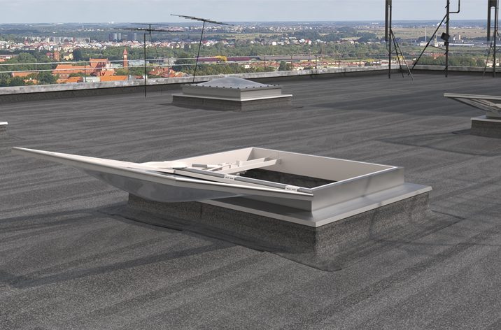 A rooftop access hatch is open on a flat, gray rooftop, overlooking a cityscape with various buildings, trees, and distant hills under a clear sky. Designed for natural ventilation, the hatch seamlessly integrates door automation for effortless operation.