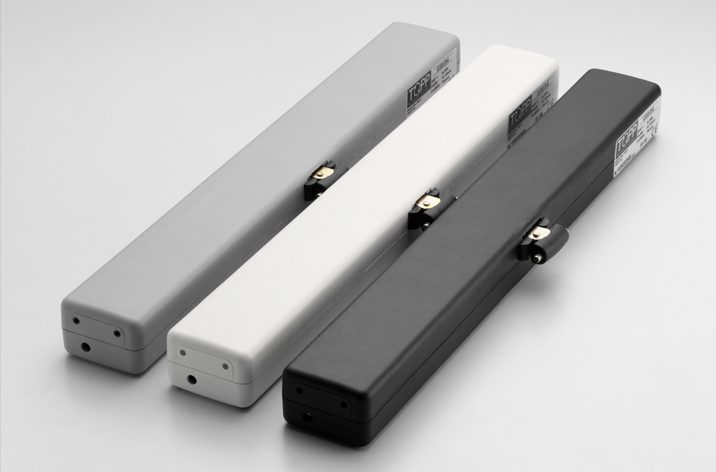 Three elongated rectangular electronic devices in gray, white, and black colors are arranged side by side on a flat surface. Each has a small switch and a label with text, ideal for integration into door automation systems.