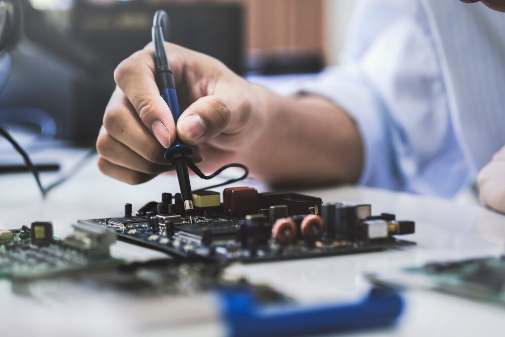 A person uses a soldering iron on an electronic circuit board, performing electronic assembly or repair work.